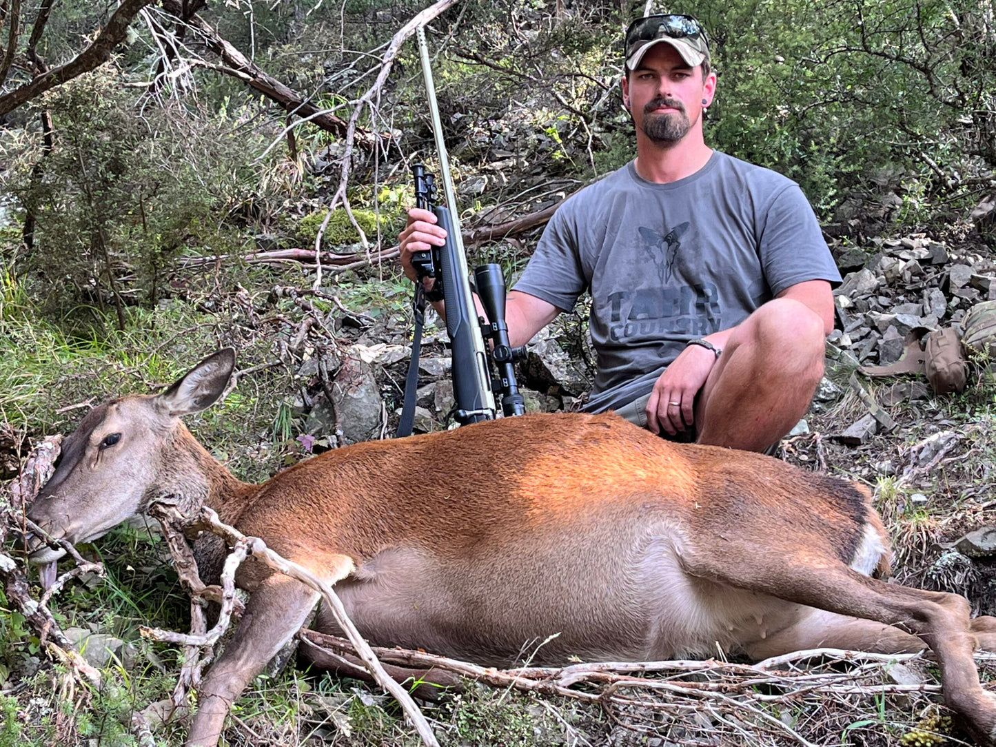 A man sitting next to a deer wearing a charcoal Tahr Country T-shirt with bold TAHR COUNTRY letters on the front with a Tahr Head image above it