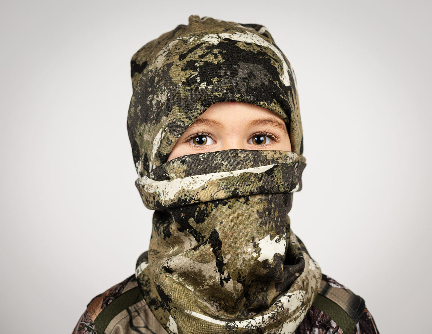 A child wearing the tahr country merino beanie and buff in camouflage with a white backdrop.